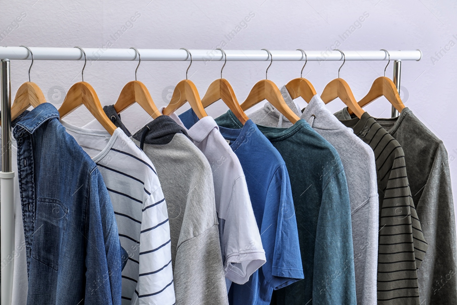 Photo of Stylish clothes hanging on wardrobe rack against light background