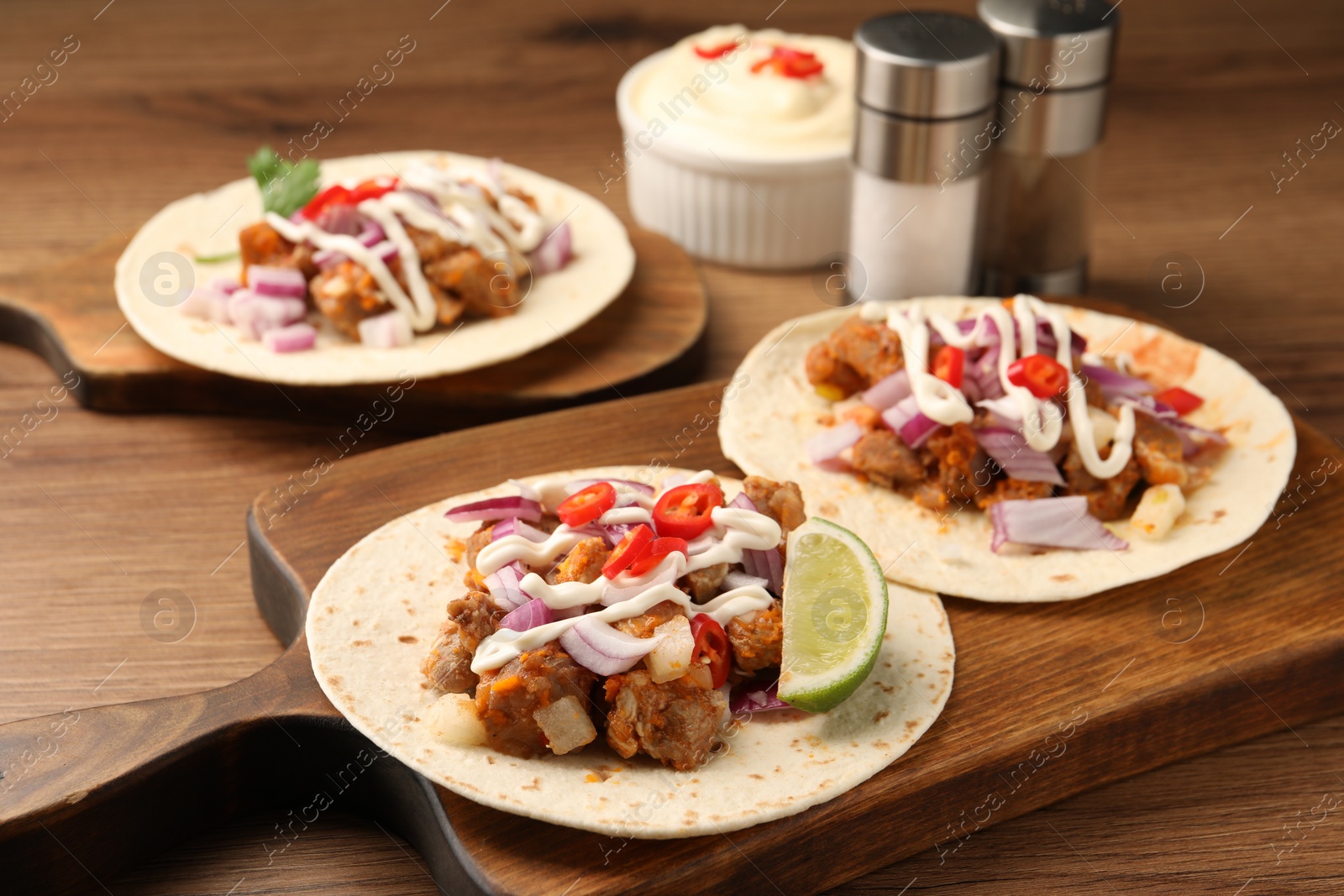 Photo of Delicious tacos with vegetables, meat and sauce on wooden table