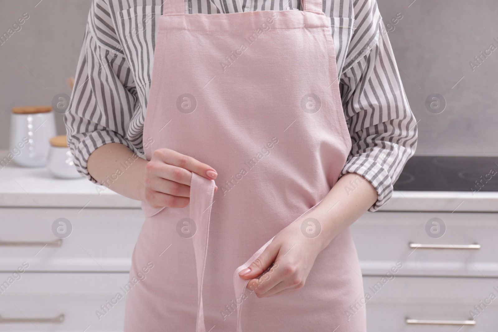 Photo of Woman putting on pink apron in kitchen , closeup