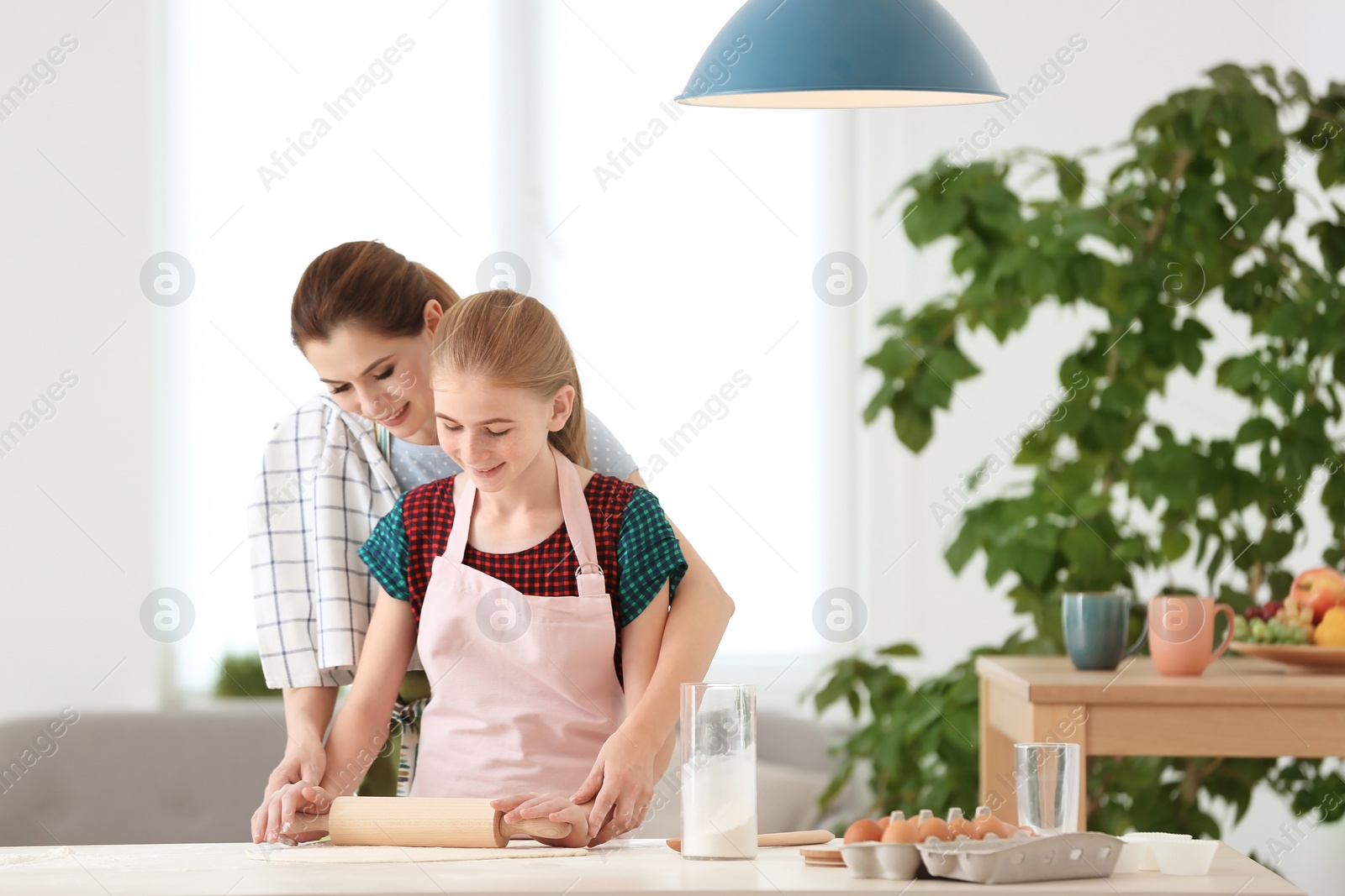 Photo of Mother and her daughter making dough at table in kitchen