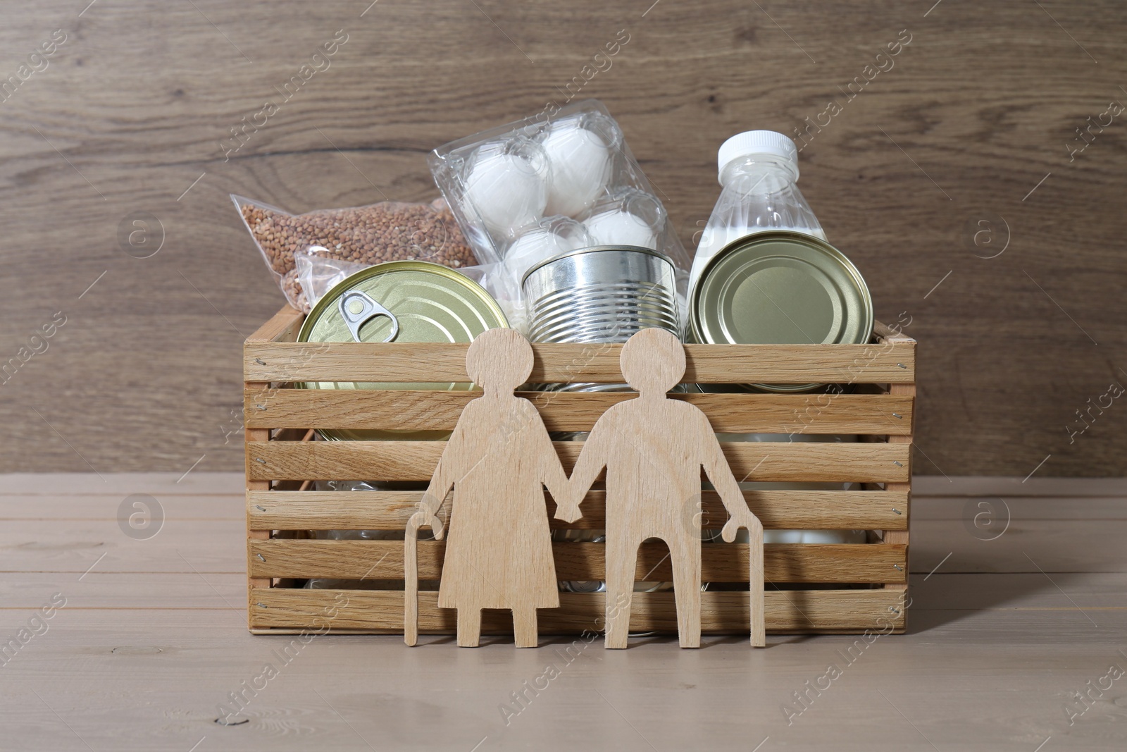 Photo of Humanitarian aid for elderly people. Donation box with food products and figure of senior couple isolated on wooden table
