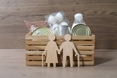 Humanitarian aid for elderly people. Donation box with food products and figure of senior couple isolated on wooden table