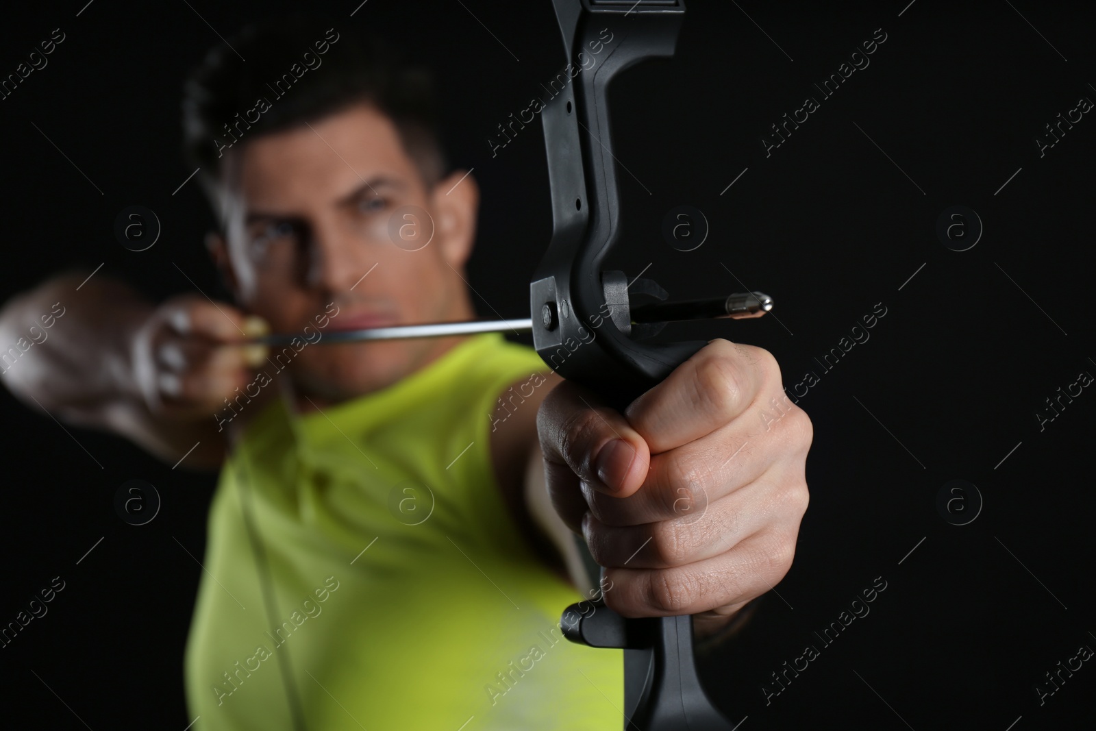 Photo of Man with bow and arrow practicing archery against black background, focus on hand