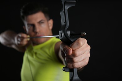 Man with bow and arrow practicing archery against black background, focus on hand