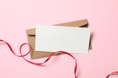 Photo of Blank card, envelope and red ribbon on pink background, flat lay with space for text. Valentine's Day celebration