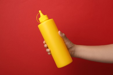 Woman with bottle of mustard on red background, closeup