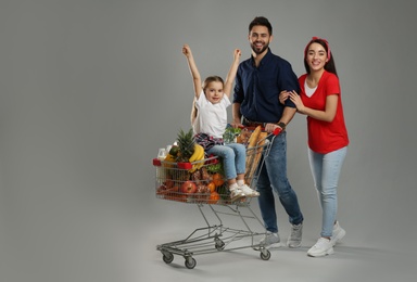 Photo of Happy family with shopping cart full of groceries on grey background