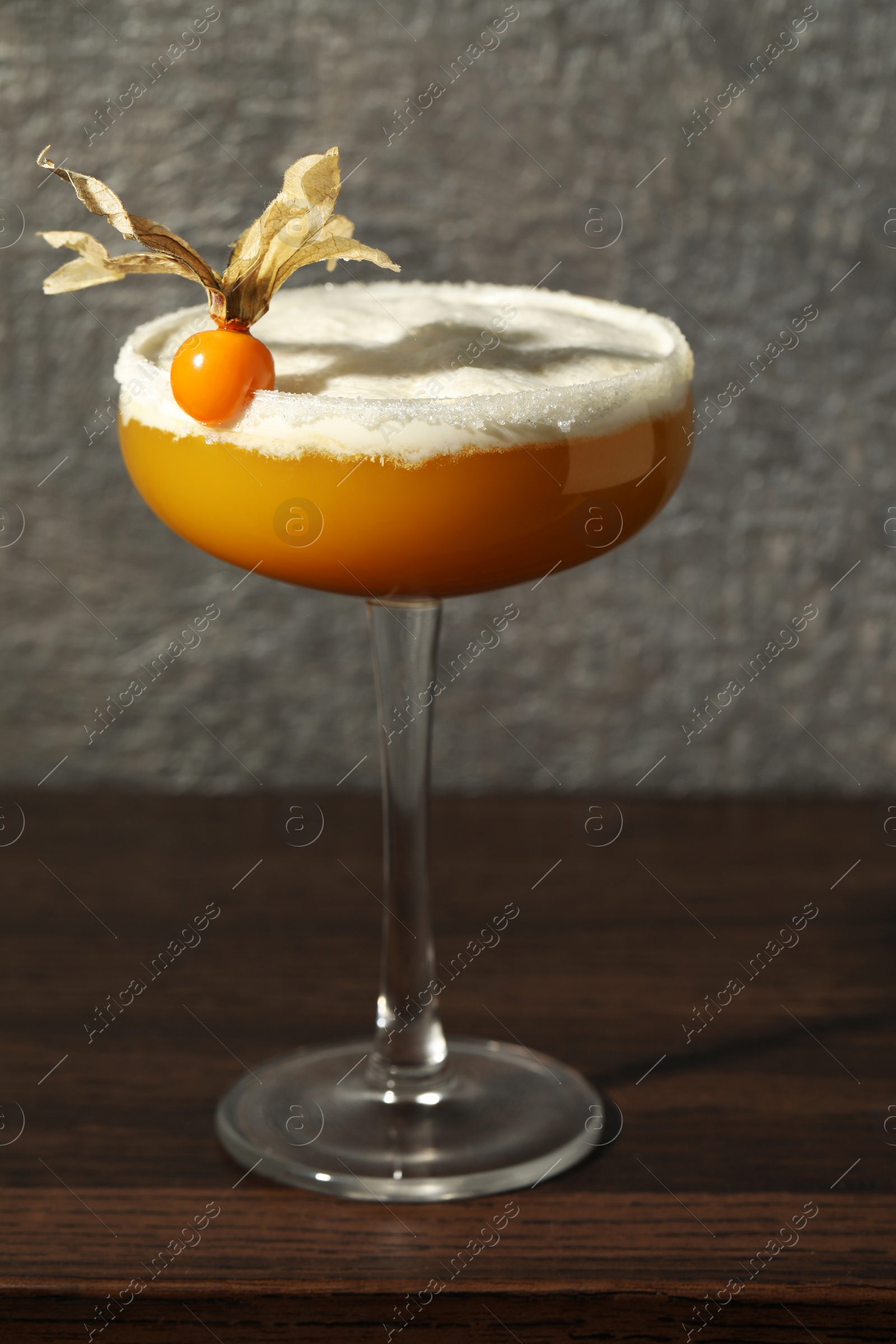 Photo of Refreshing cocktail decorated with physalis fruit on wooden table near grey wall