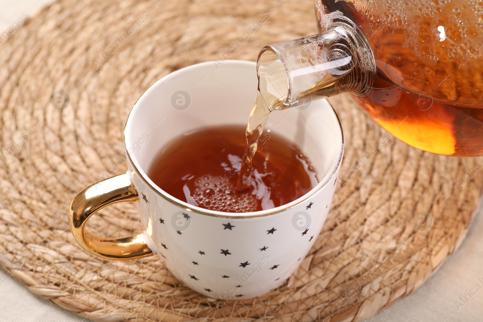 Photo of Pouring aromatic tea into cup at table, closeup