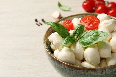 Photo of Delicious mozzarella balls, tomatoes and basil leaves in bowl on white wooden table, closeup. Space for text