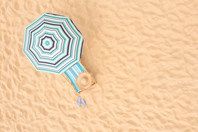 Image of Striped beach umbrella near sunbed with vacationist's stuff on sandy coast, aerial view. Space for text