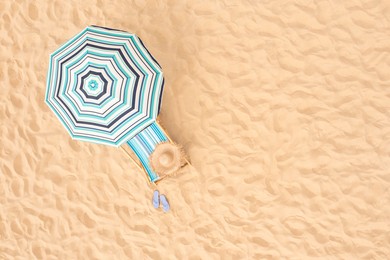 Striped beach umbrella near sunbed with vacationist's stuff on sandy coast, aerial view. Space for text