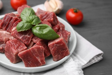 Photo of Cut fresh beef meat with basil leaves on grey table, closeup