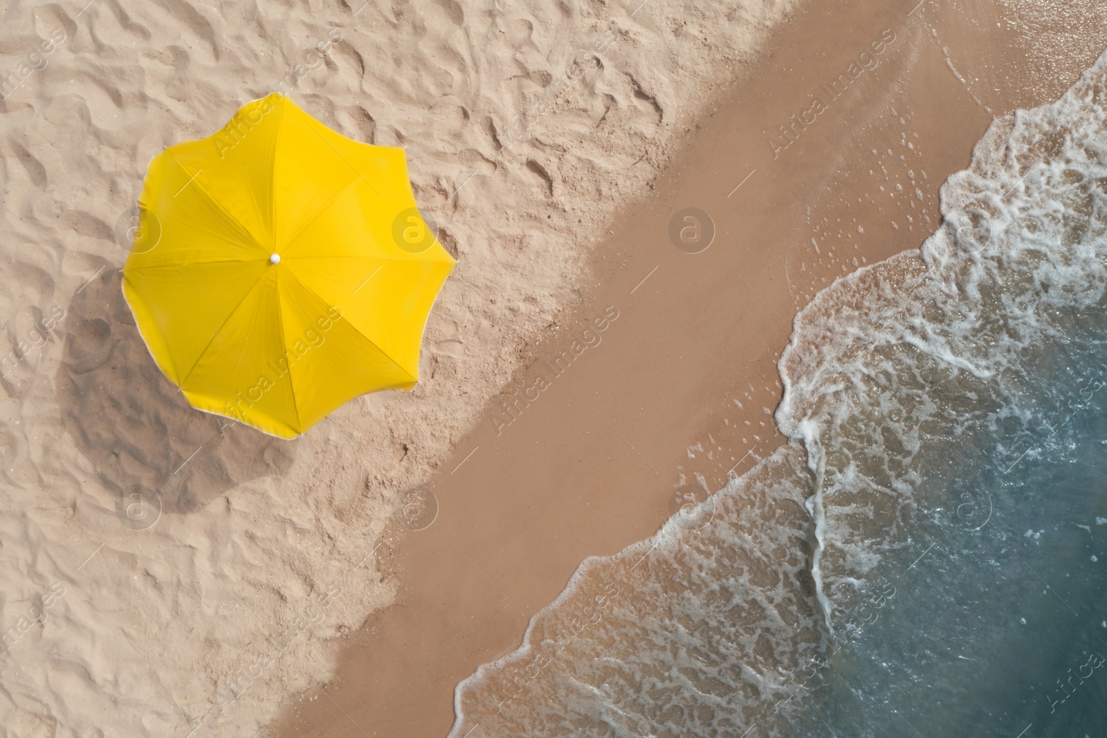 Image of Yellow beach umbrella on sandy coast near sea, top view