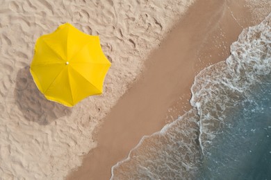 Yellow beach umbrella on sandy coast near sea, top view