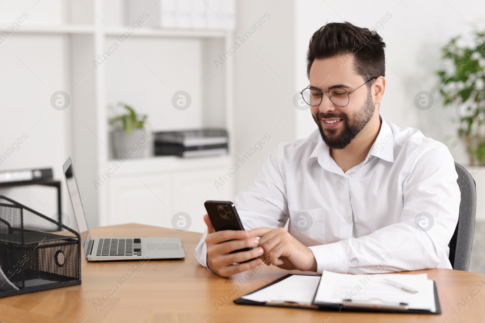 Photo of Handsome young man using smartphone at wooden table in office