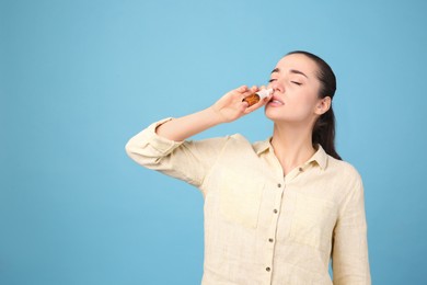 Woman using nasal spray on light blue background, space for text