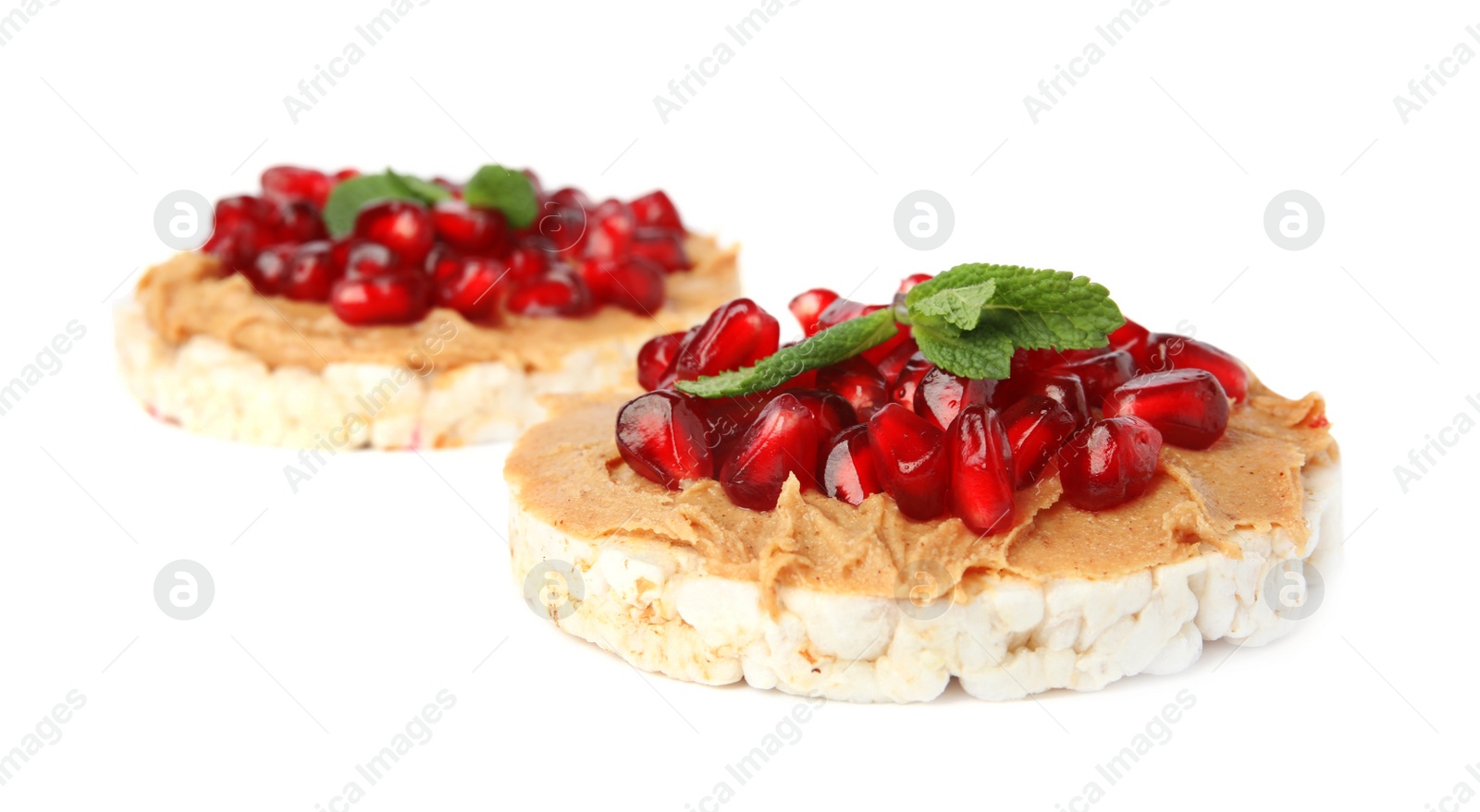 Photo of Puffed rice cakes with peanut butter, pomegranate seeds and mint isolated on white