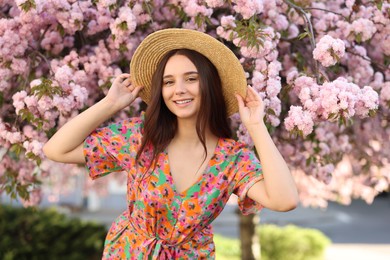 Photo of Beautiful woman in straw hat near blossoming tree on spring day