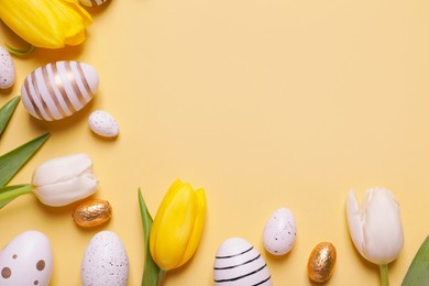 Flat lay composition of painted Easter eggs and tulip flowers on yellow background. Space for text