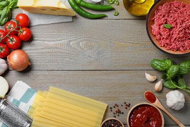 Frame made of fresh lasagna ingredients on grey wooden table, flat lay. Space for text