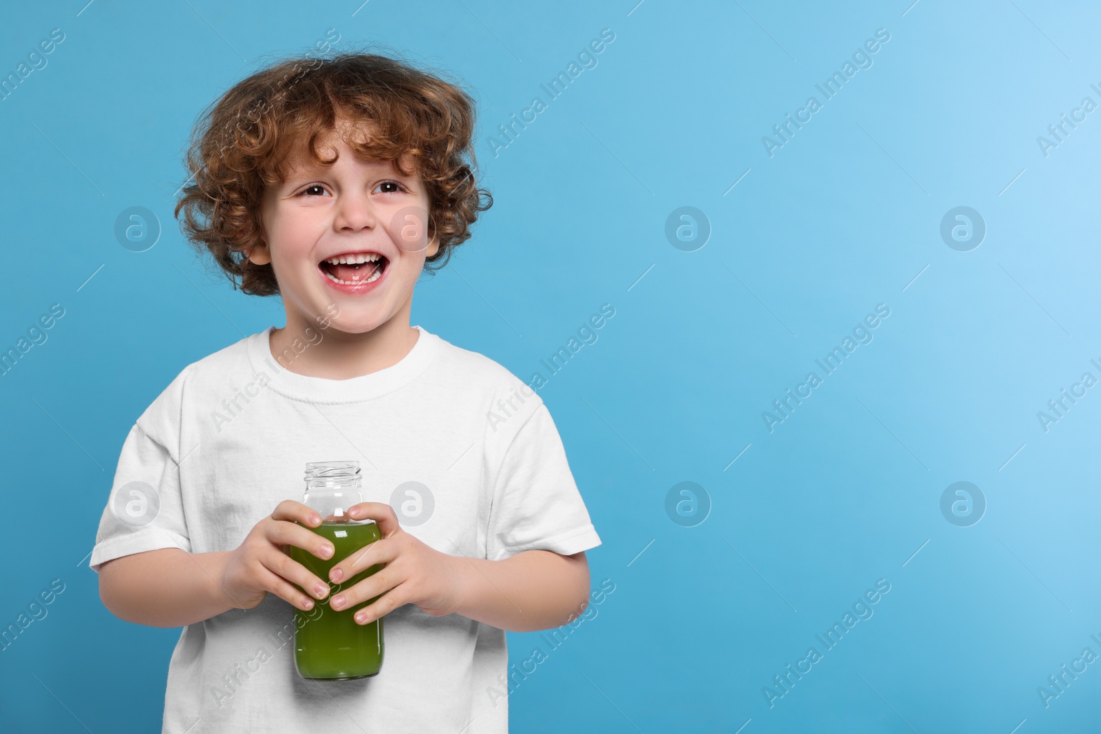 Photo of Cute little boy with glass bottle of fresh juice on light blue background, space for text