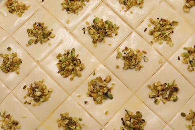 Photo of Making delicious baklava. Raw dough with pistachios as background, top view