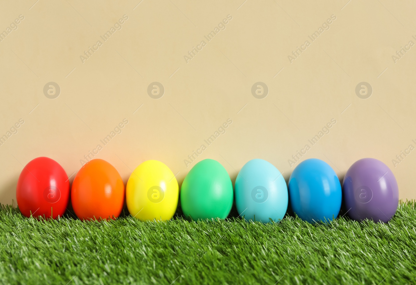 Photo of Bright Easter eggs on green grass against beige background