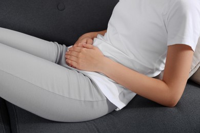 Photo of Woman suffering from cystitis on sofa at home, closeup