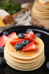 Photo of Delicious pancakes with strawberries and blueberries on black plate, closeup