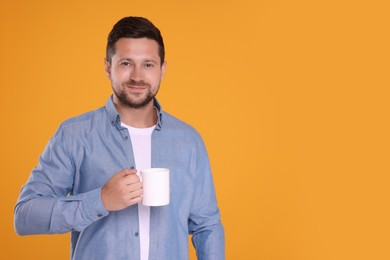 Photo of Portrait of happy man holding white mug on orange background. Space for text