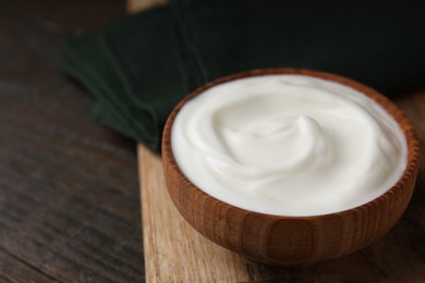 Photo of Delicious natural yogurt in bowl on wooden table, closeup. Space for text