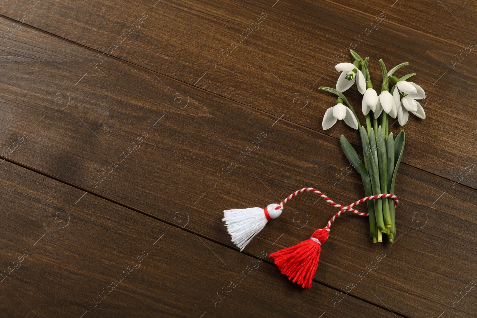 Photo of Beautiful snowdrops with traditional martisor on wooden table, flat lay and space for text. Symbol of first spring day