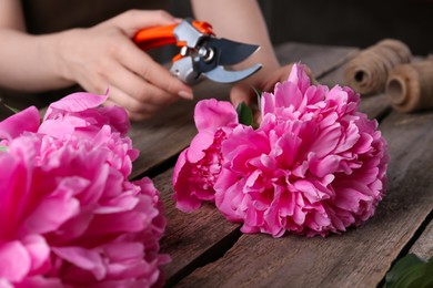 Photo of Woman trimming beautiful pink peonies with secateurs at wooden table, selective focus