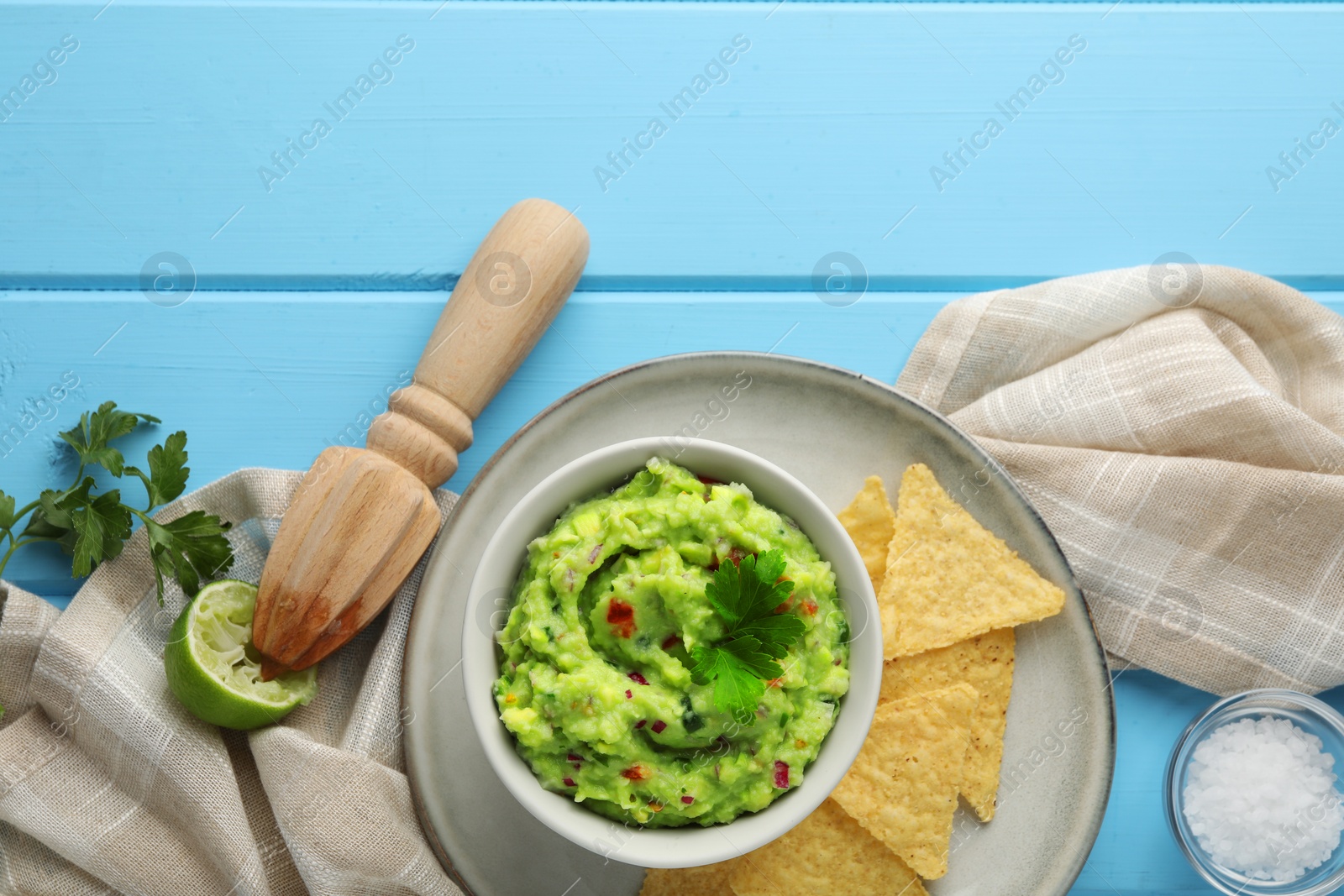 Photo of Delicious guacamole served with nachos chips on light blue wooden table, flat lay