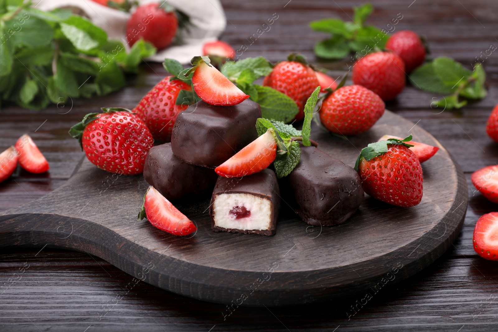 Photo of Delicious glazed curd snacks, mint leaves and fresh strawberries on wooden table, closeup