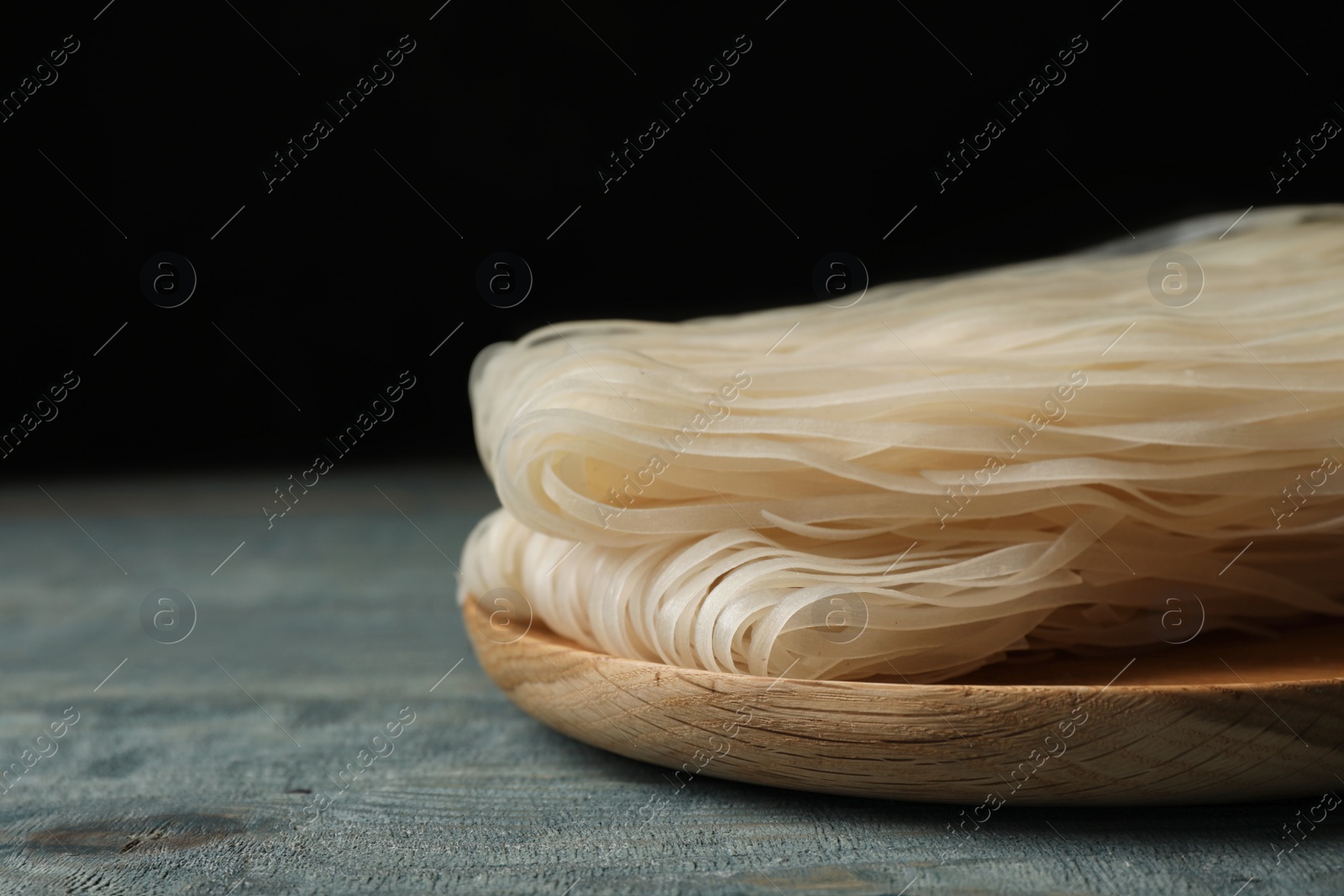 Photo of Plate with raw rice noodles on wooden table, closeup. Space for text