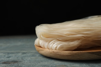 Plate with raw rice noodles on wooden table, closeup. Space for text