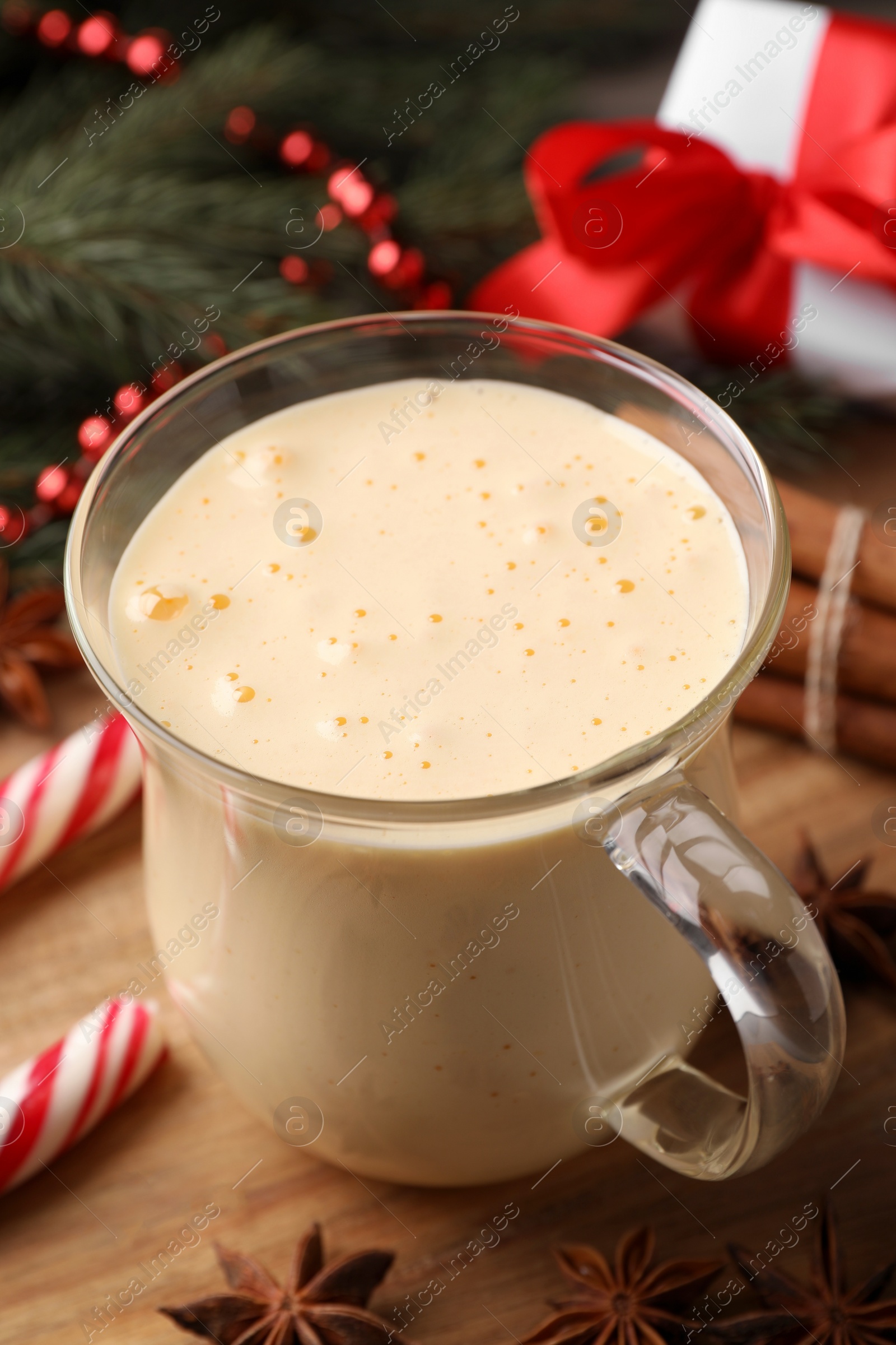 Photo of Glass of delicious eggnog on wooden table, closeup