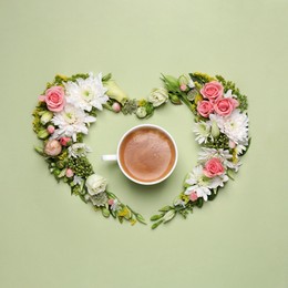 Photo of Beautiful heart shaped floral composition with cup of coffee on light green background, flat lay