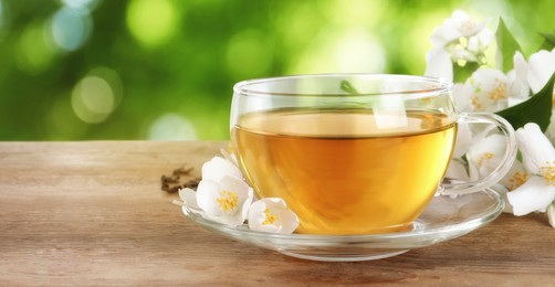 Image of Cup of jasmine tea and fresh flowers on wooden table outdoors, space for text. Banner design