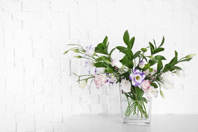 Vase with bouquet of beautiful flowers on table near brick wall. Space for text