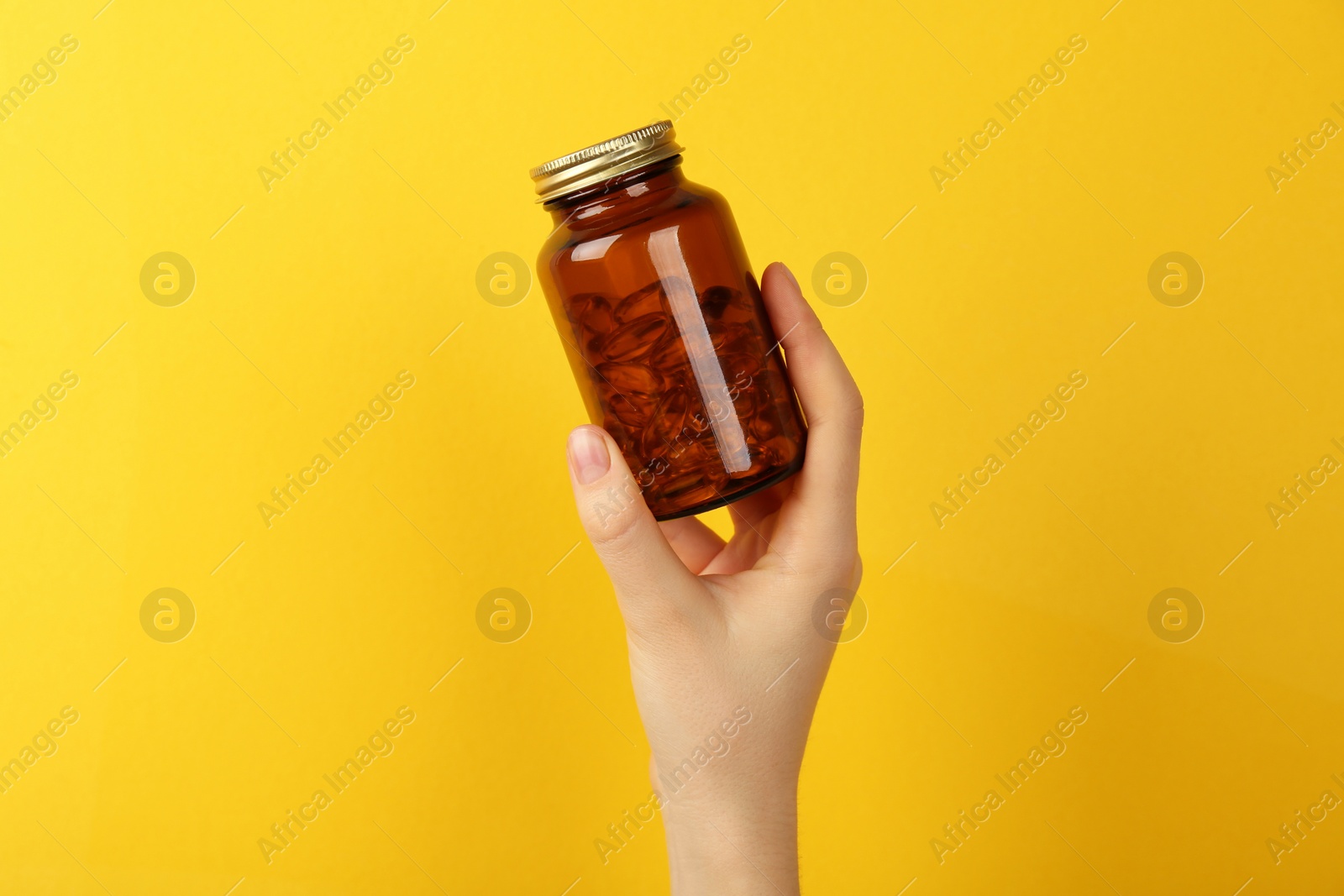 Photo of Woman holding jar with vitamin capsules on yellow background, closeup