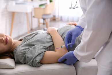 Doctor giving injection to pregnant woman in hospital, closeup. Vaccination concept