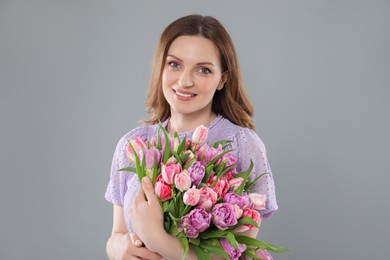 Photo of Happy young woman with bouquet of beautiful tulips on grey background