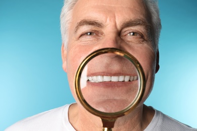 Photo of Mature man with healthy teeth and magnifier on color background, closeup