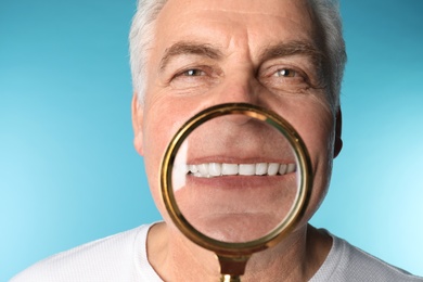 Mature man with healthy teeth and magnifier on color background, closeup