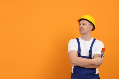 Worker holding paint brush near orange wall. Space for text