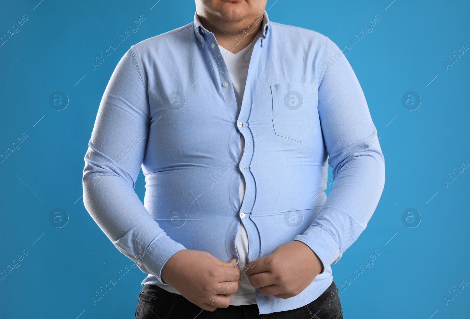 Photo of Overweight man trying to button up tight shirt on light blue background, closeup