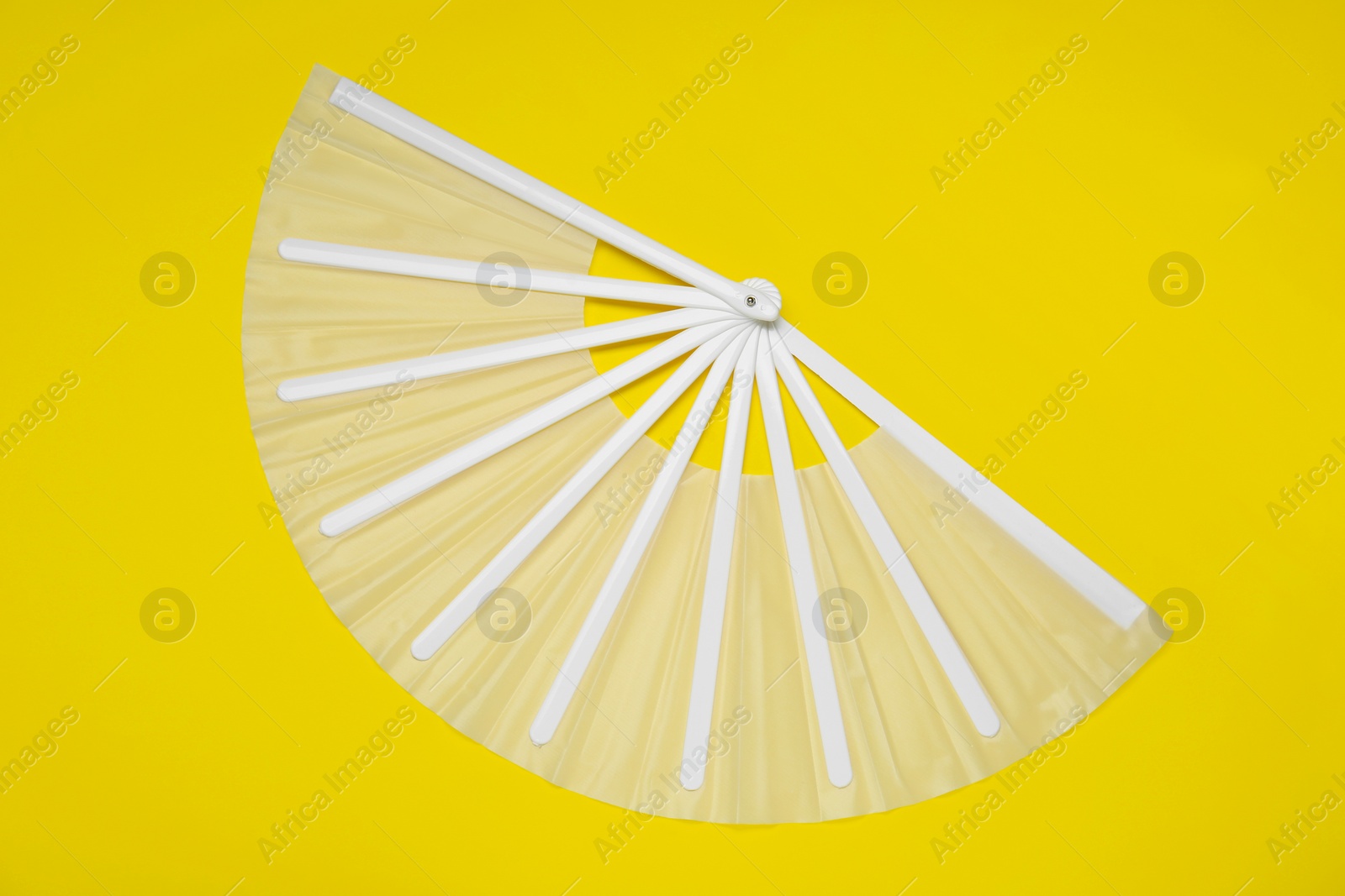 Photo of White hand fan on yellow background, top view